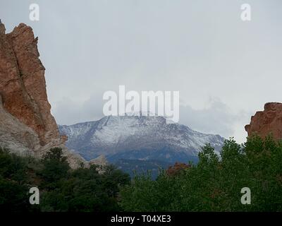 Rock walls with trees and bushes at the Garden of the Gods, with the snow-capped Pikes Peak in the background in Colorado Springs, Colorado. Stock Photo