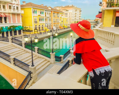 Aerial view of elegant woman looking Venice bridge in Doha, Qatar at twilight. Qanat Quartier in the Pearl, Persian Gulf, Middle East. Scenic Stock Photo