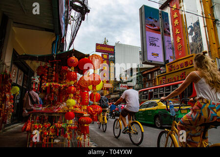Tourists strolling with yellow bicycles through the chaotic streets of Chinatown in Bangkok, Thailand Stock Photo
