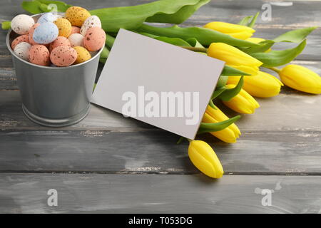 Colorful easter candy eggs with yellow tulips and empty greeting card on wooden table Stock Photo