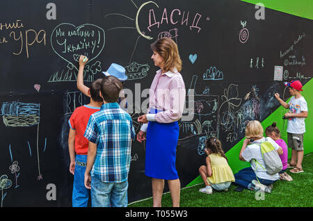 Dnipro, Ukraine - June 27, 2018: Marina Poroshenko with children draws scrawl chalk on a blackboard in inclusive gaming park of the city Stock Photo