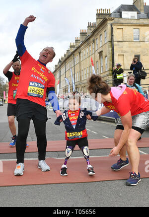 Five-year-old Harmonie-Rose Allen, who lost her limbs to meningitis, crossing the finishing line in the Bath Half Marathon with the help of her teacher Antony Wainer and her auntie Hannah Hall. Stock Photo