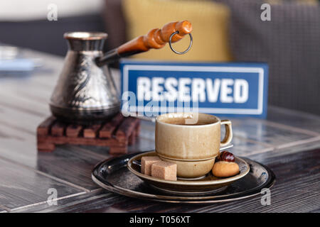 Closeup breakfast with Turkish coffee in cezve on wooden stand, porcelain cup with sugar cubes served on table in restaurant, reserved plate. Сoncept  Stock Photo