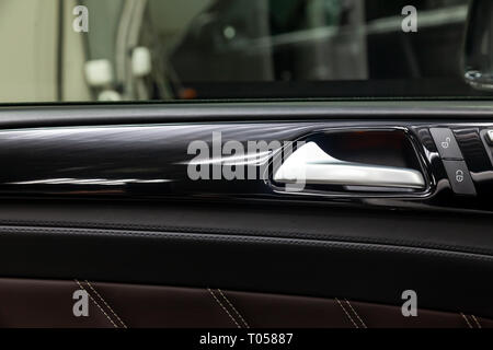 A close-up view of a part of the interior of a modern luxury car with a view of a silver-colored door handle on a chrome finish with black wood trim Stock Photo