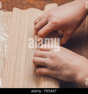 A female cook prepares sushi in the kitchen and wraps a letter to the nori in the roll 2019 Stock Photo