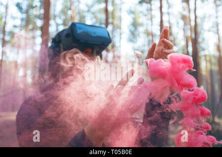 A woman wearing virtual reality goggles in the forest sees smoke bombs. VR glasses. Stock Photo