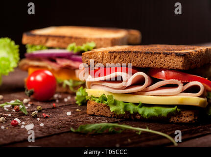 Fresh delicious toasts with cheese, tomato, onion, ham, prosciutto, cucumber and lettuce on wooden table and dark background Stock Photo