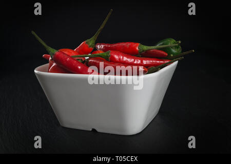 Various Red Hot Chili Peppers in a white bowl over a dark background. Stock Photo