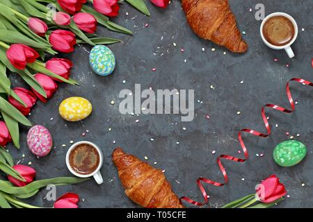 Easter background. Tulips with coffee, colorful eggs and croissant. Top view with copy space. Stock Photo