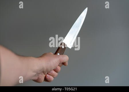 Man's hand with a knife on gray background. Concept of violence. Stock Photo