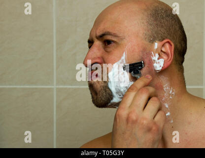 Man shaving his face with the razor blade through shave foam. Men skin care concept. Bald Stock Photo