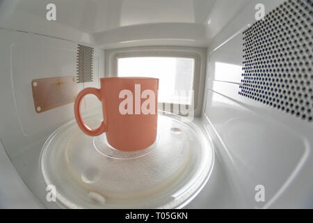 A mug standing on a microwave plate. Device for heating dishes with the use of myocual waves. Light background. Stock Photo