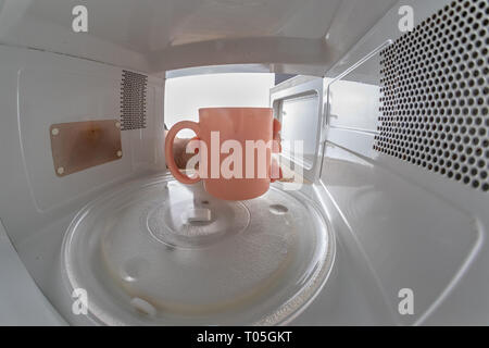 A mug standing on a microwave plate. Device for heating dishes with the use of myocual waves. Light background. Stock Photo