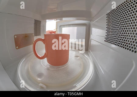 A mug standing on a microwave plate. Device for heating dishes with the use of myocual waves. Light background. Stock Photo