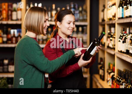 Image of two women with bottle of wine in store on background of shelves Stock Photo