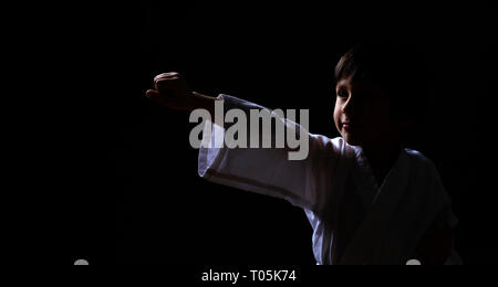 A karate boy in white kimono posing on dark background. Child ready for martial arts fight. Kid fighting at Aikido training. Best for martial fights a Stock Photo