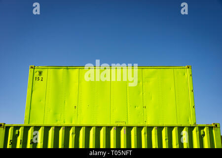 A stack of colorful green shipping containers against a blue sky, horizontal Stock Photo