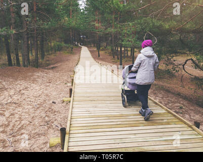 woman with stroller walking on wooden pedestrian path in forest Stock Photo
