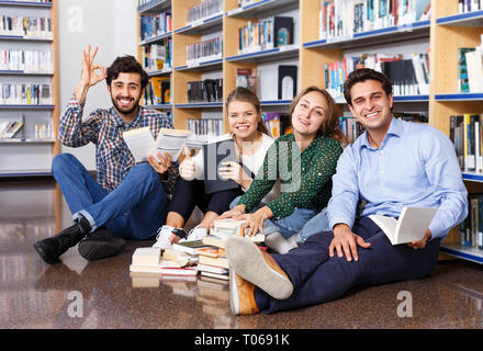 Cheerful group of students reading textbooks together while sitting on floor in university library Stock Photo