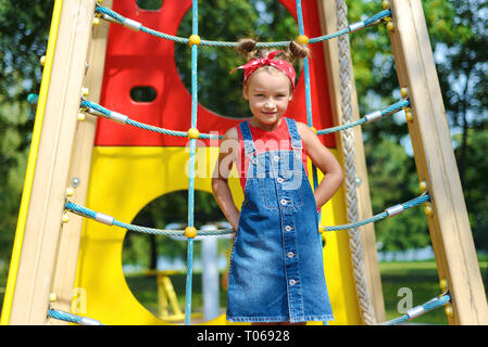 portrait of beautiful little girl in denim suit and red T-shirt on children's playground Stock Photo