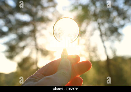 A male hand holds a magnifying glass against the setting sun outside. concept of search, creative thinking and use of solar energy Stock Photo