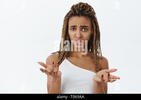 Woman feeling confused cannot understand what friend hinting at. Portrait of clueless and questioned unaware dark-skinned female with dreads feeling Stock Photo