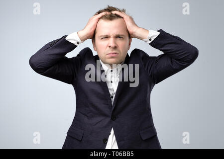 Doubtful handsome man in suit standing touching his head and looking at caemra, thinking. Stock Photo