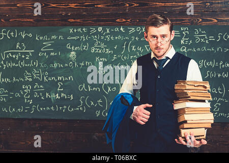 Young student in suit and glasses walking to library with heap of books. Bookworm studying for exam Stock Photo