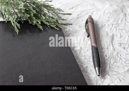 Top view on black note pad with green branch and pens on white desk background for mockup. There is a place for your text. Stock Photo