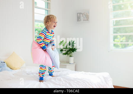 Child playing in bed in white sunny bedroom with window. Kids room and interior design. Baby boy at home. Bedding and textile for children nursery. Ki Stock Photo