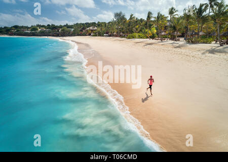 Aerial view of the running young woman on the white sandy beach near sea with waves at sunrise. Summer holiday. Top view of sporty slim girl, clear az