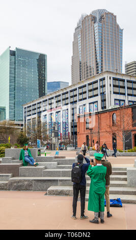 CHARLOTTE, NC, USA-3/16/19: High school graduates taking pictures in first ward park, with city skyline behind. Stock Photo