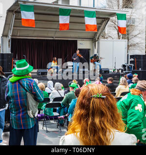 CHARLOTTE, NC, USA-3/16/19: A red-haired woman stands and listens to an Irish music band on St. Patrick's Day in uptown Charlotte. Stock Photo