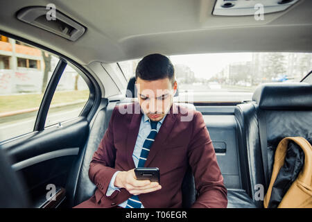 Handsome bearded business man in suit using mobile phone in the back seat of a car Stock Photo