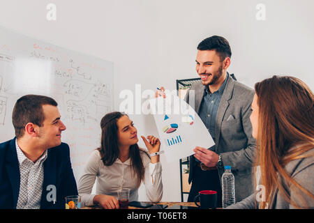 Young architect is in the office, he is showing a diagram to his colleagues Stock Photo
