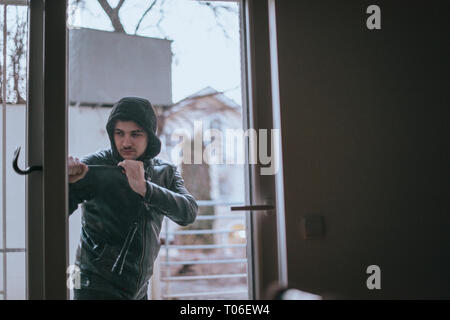 Housebreaker wearing black clothes and leather coat breaking in a house Stock Photo