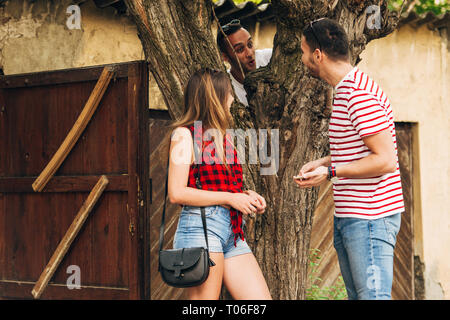 Three friends having fun  outside, near by an old ruining house while one of them is trying to climb to a tree Stock Photo
