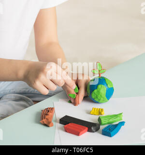 The child sculpts from plasticine the globe and trees. The location of the planet in children's palms. Ecology concept. Stock Photo