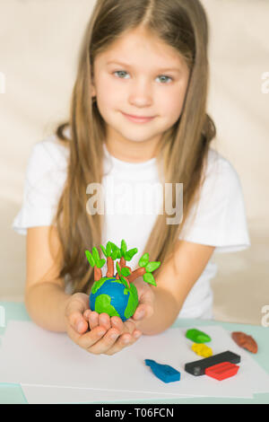 A little girl holds in her hands a model globe with trees made of plasticine. A small globe lies in the palms of child. Stock Photo