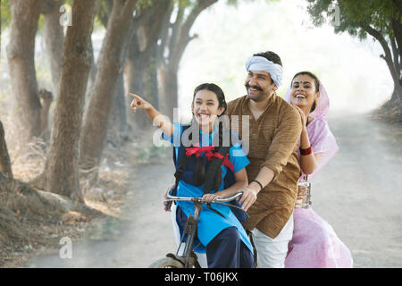 Happy rural couple along with their daughter riding on bicycle in village. Stock Photo