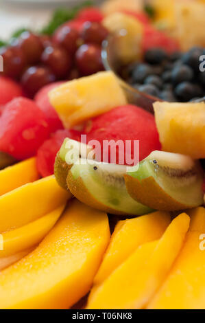 Fresh fruit arranged on a platter as slices, cubes, balls, and whole pieces, vertical orientation Stock Photo