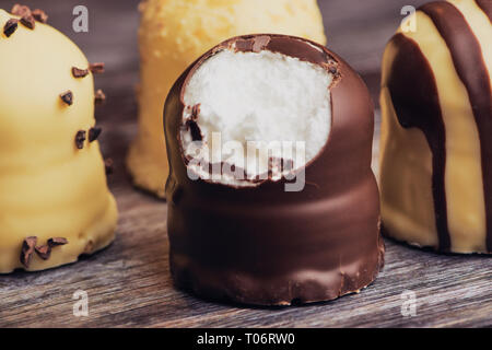 group of white and dark chocolate covered marshmallows. one is bitten off, on a brown wooden background Stock Photo