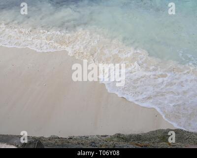 White foaming waves gently lapping against the soft white sand beach in a tropical island Stock Photo