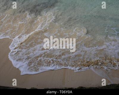 Close up of white foaming waves gently lapping against a soft sandy beach in a tropical island Stock Photo