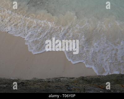Beautiful patterns of foaming waves gently lapping against the soft white sand beach in a tropical island Stock Photo