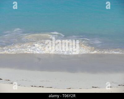 Waves rolling gently against the soft white sand create stunning patterns of foam in a tropical beach Stock Photo