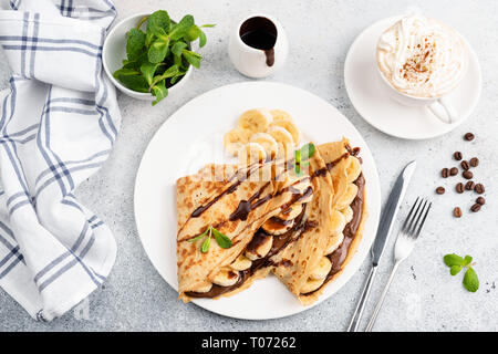 Crepes with banana, chocolate and cup of cappucino on concrete background. Top view sweet breakfast food Stock Photo