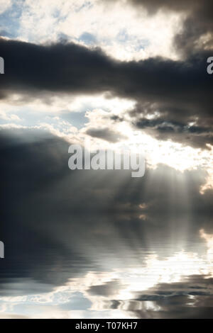 bright sun rays coming through the clouds and falling on sea water Stock Photo