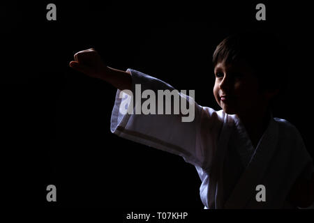 Karate boy in white kimono posing on dark background. Child ready for martial arts fight. Kid fighting at Aikido training. Best for martial fights and Stock Photo