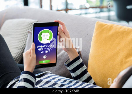Woman lying down on sofa using tablet ask question chat bot at home.digital technology lifestyle Stock Photo